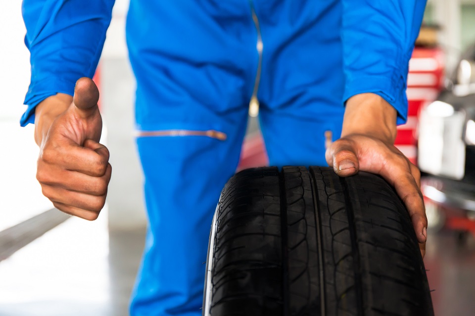 Mechanic holding a car wheel with thumb up sign in car garage service