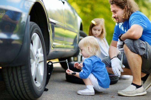 Adorable little girl helping her father to change a car wheel outdoors on beautiful summer day